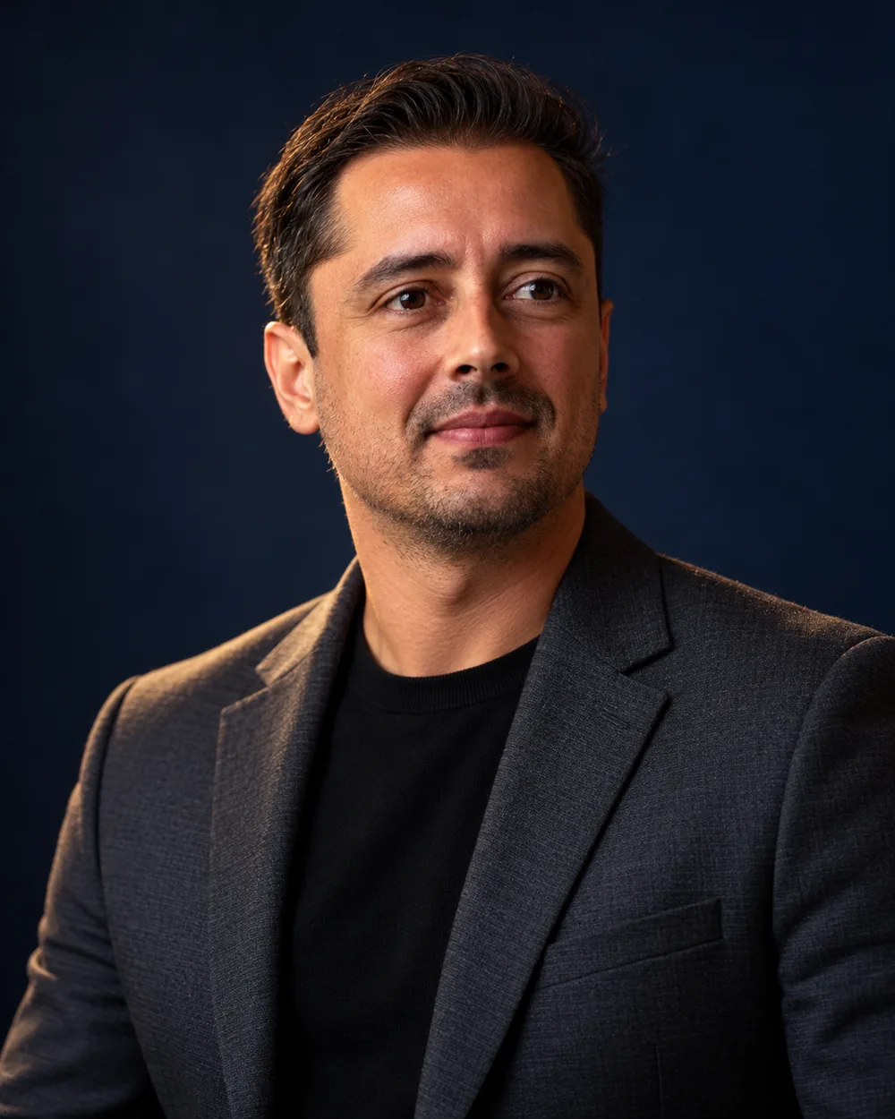 Retrato de Felipe Gabriel, de blazer escuro e camiseta preta, em fundo azul-noite